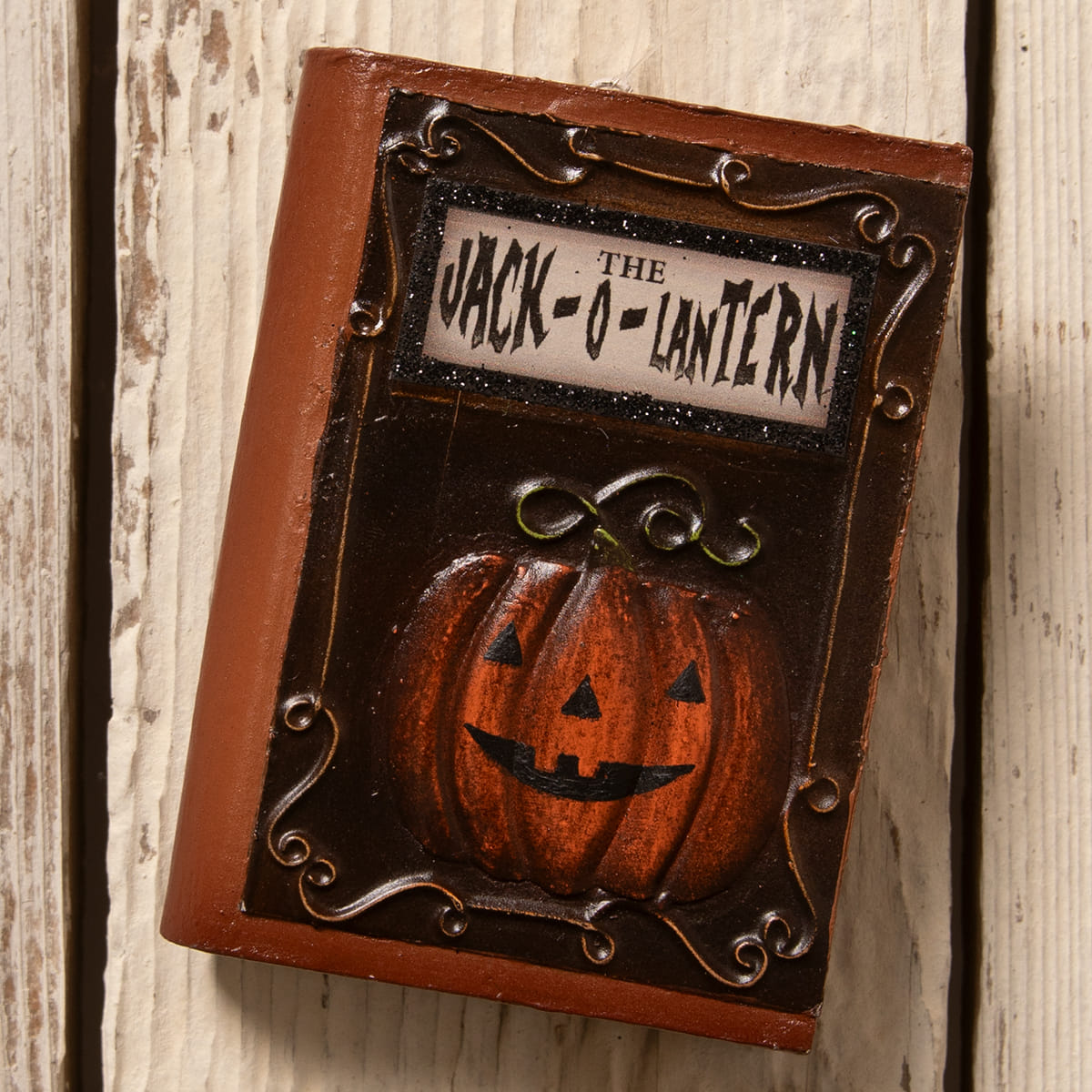 A rustic bethany lowe jack o lantern book ornament magnet with a carved orange pumpkin and metal scrollwork frame