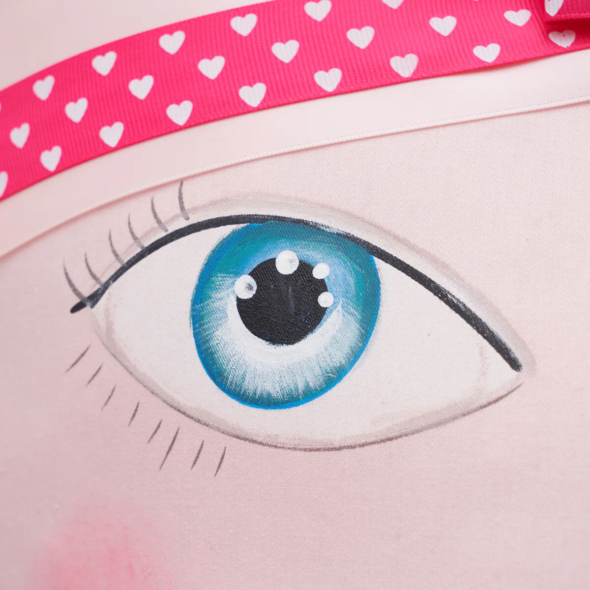 A pink fabric zombinaland decorative pillow with a blue eye illustration framed by a bright pink heart ribbon