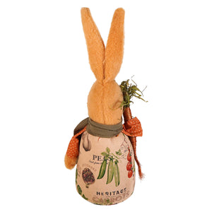 A plush orange jeffrey rabbit holding carrot figurine wearing a fabric apron with vegetable prints