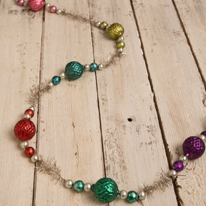 A festive jewel-tide glass bead garland with shiny red green teal and purple glass ornaments and silver tinsel accents