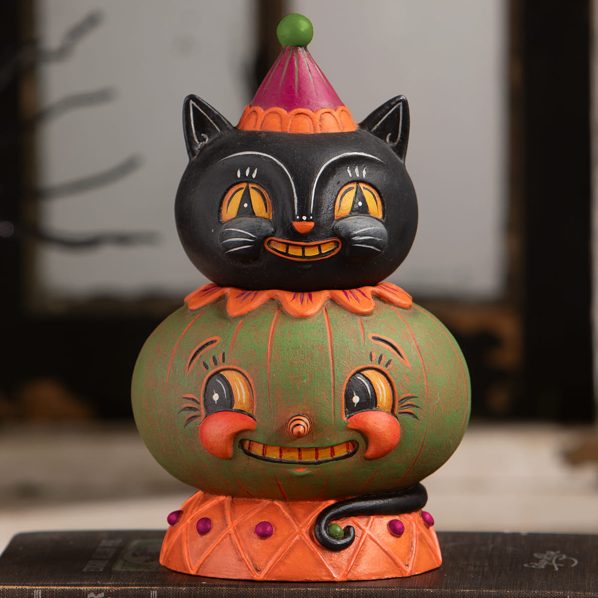 A whimsical jolly jack-a-melon stack with a black cat figurine wearing a party hat on a smiling green jack o lantern base