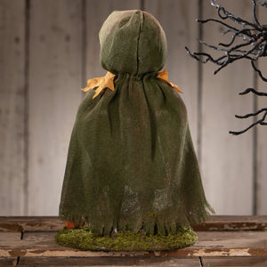 A rustic olive green burlap hooded cloak with frayed edges and dried orange leaves on a mossy base for halloween figural decor pumpkin