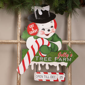 A cheerful vintage wooden snowman ornament with black top hat and green scarf on bethany lowe jollys tree farm sign