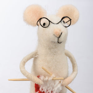 A charming cream-colored felt merry mouse critter wearing black-rimmed glasses and holding wooden knitting needles