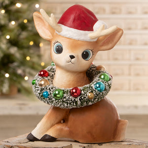 A large bethany lowe ceramic christmas reindeer figure wearing a red santa hat with frosted greenery wreath