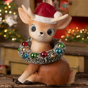 A large tan ceramic reindeer figurine by bethany lowe design wearing a red santa hat with festive wreath decor