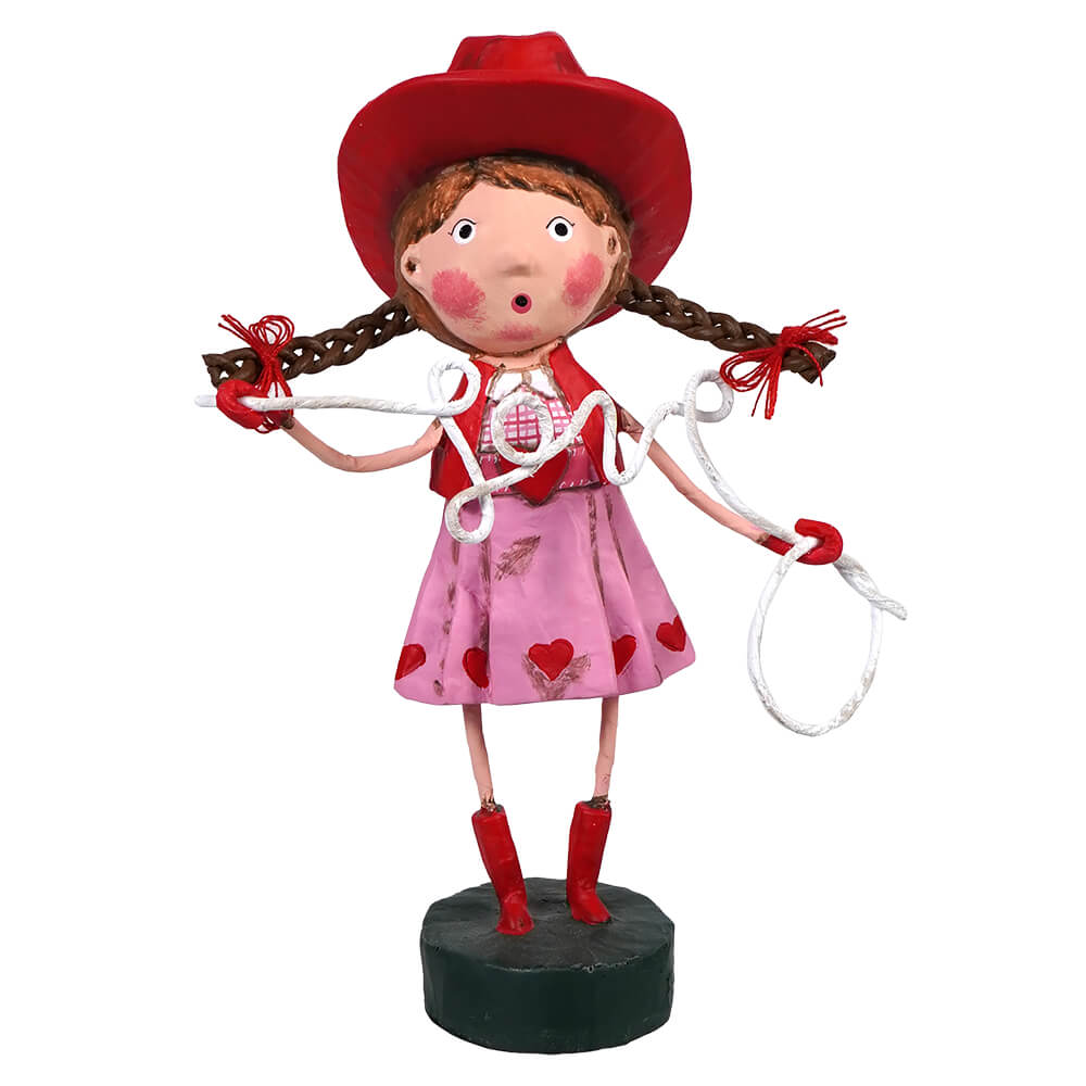 Whimsical cowgirl figurine with braided pigtails wearing a red hat, pink dress with hearts, and holding a lasso.