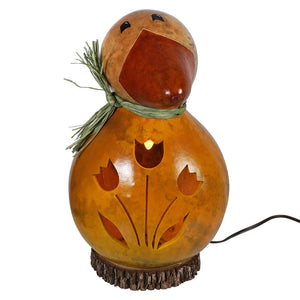 A warmly lit large dillard duck gourd lamp with amber glow carved tulip patterns and green straw scarf