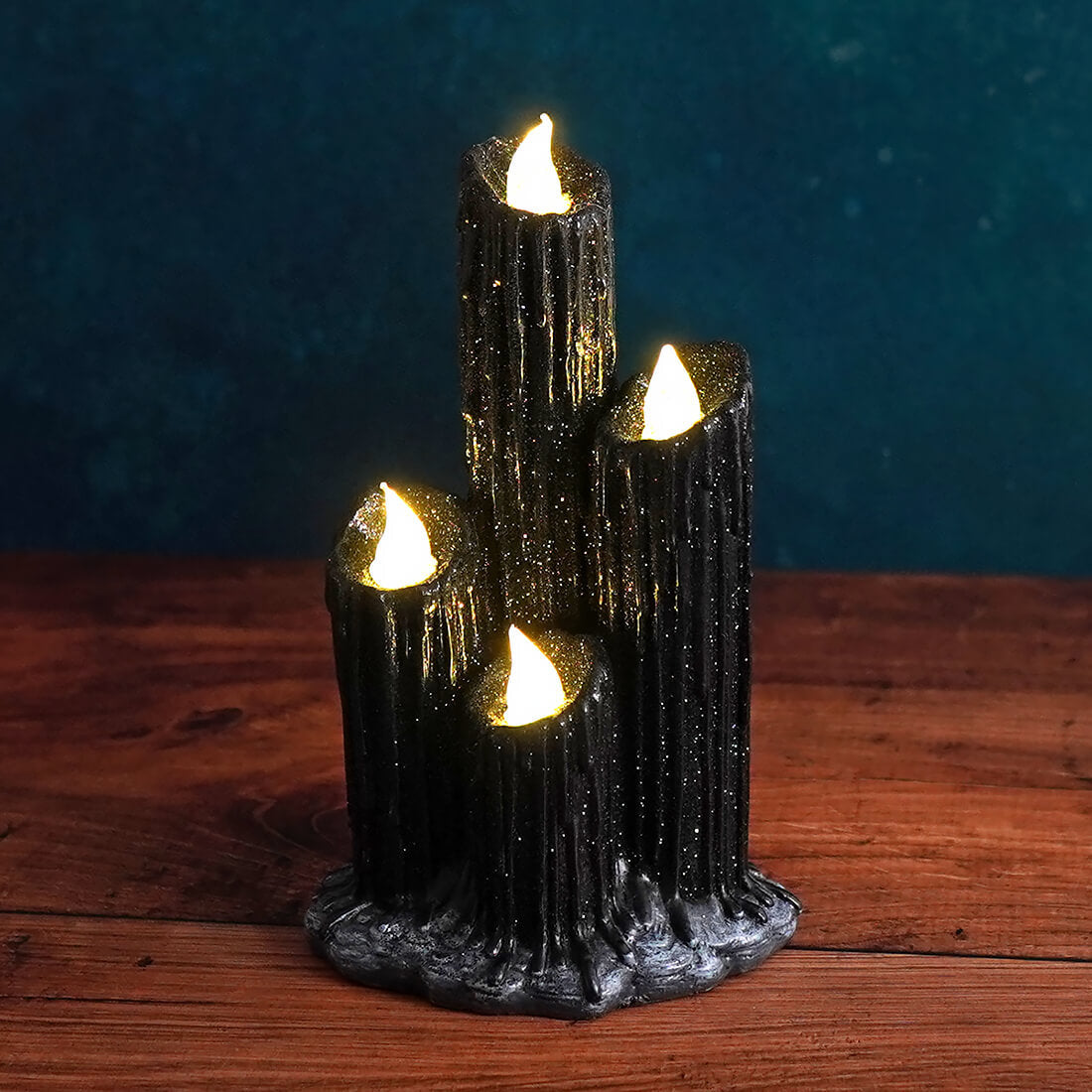 Cluster of four black dripping candles with glowing tips on a shared base.