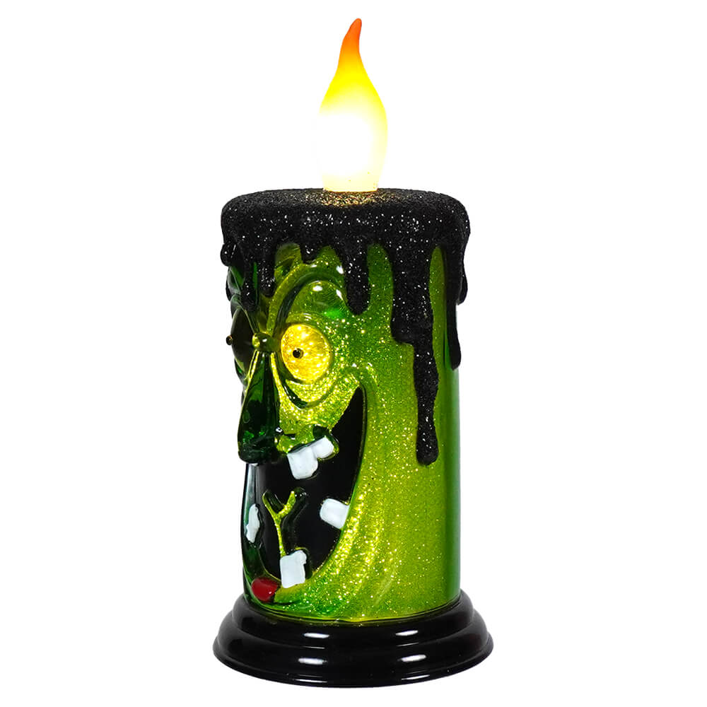 Spooky green candle with a monstrous face and glowing flame.