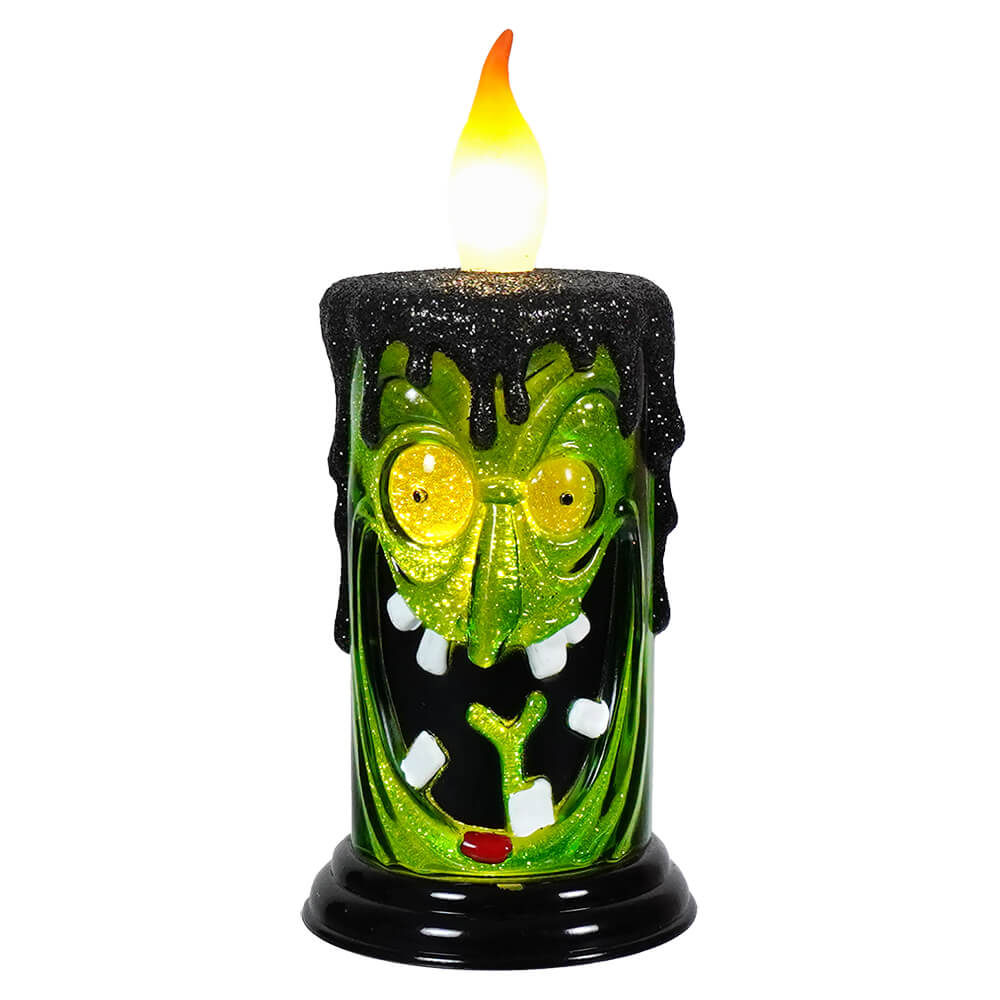 Halloween-themed decorative candle shaped like a green monster face with glowing eyes and fangs.