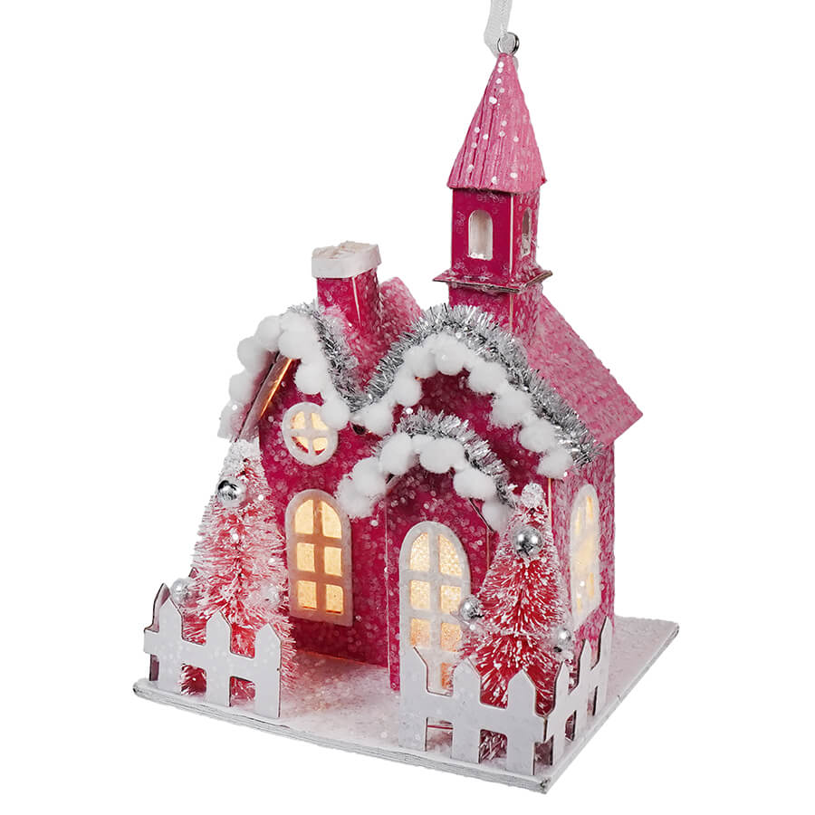 Pink Christmas-themed decorative house with snow-covered roof, illuminated windows, and a small steeple.