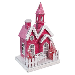 Pink glittery Christmas house decoration with snow-covered roof and white picket fence.