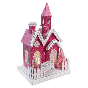 Pink glittery Christmas house decoration with snow-covered roof and a small tower.