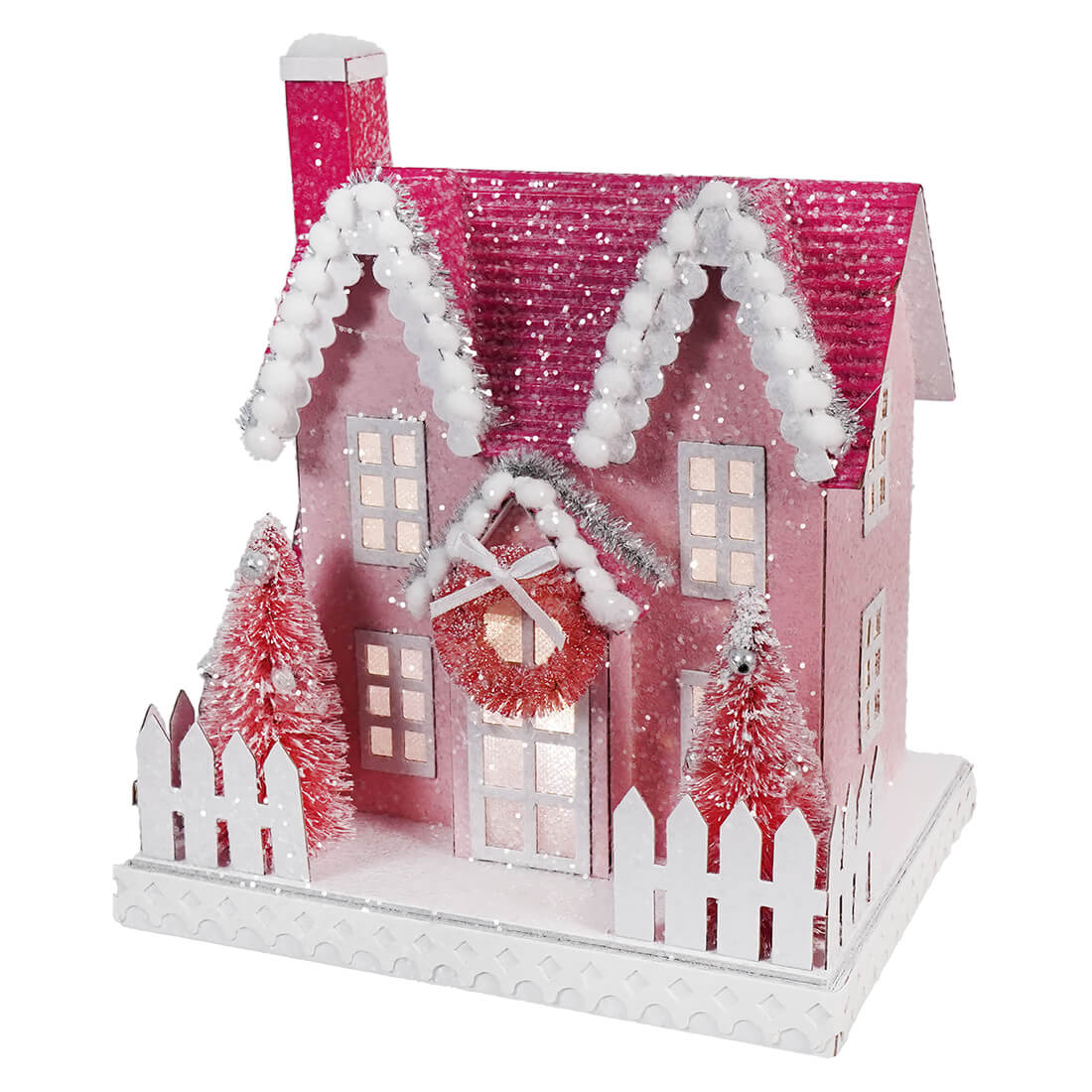 Pink and white miniature Christmas house with snowy decorations and small red trees.