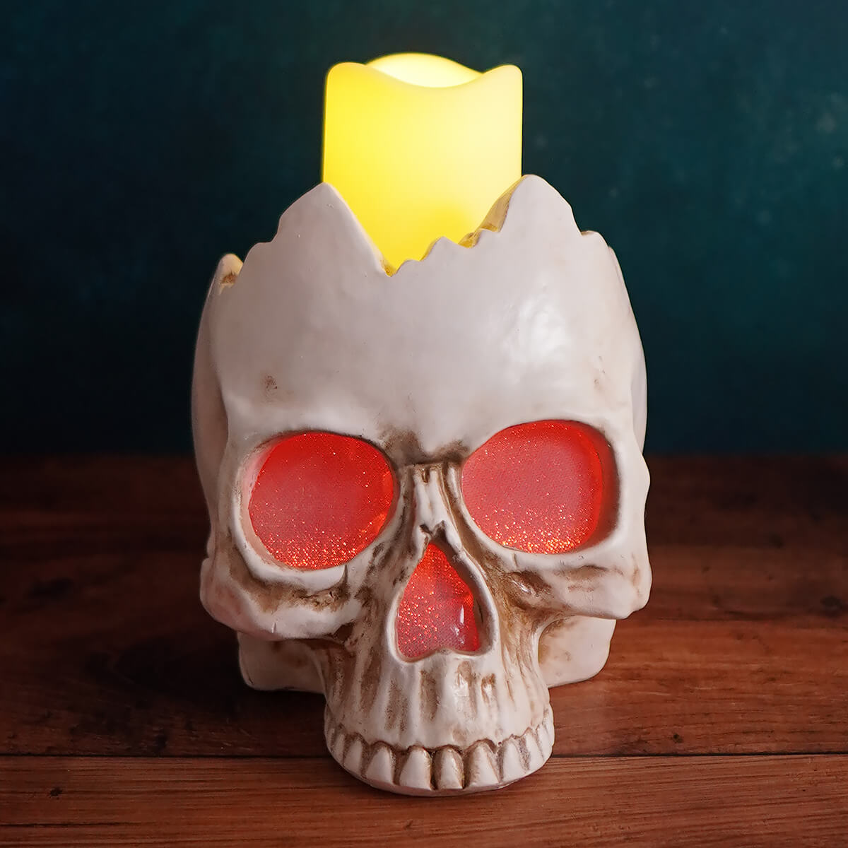 Skull-shaped candle holder with glowing yellow wax and red eye sockets.