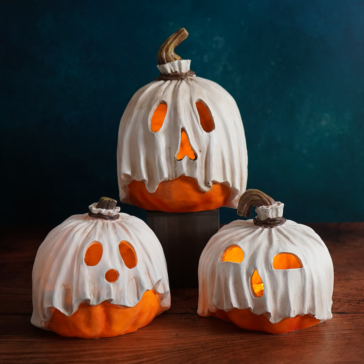 Three white ceramic ghost pumpkins with glowing orange interiors and carved faces.