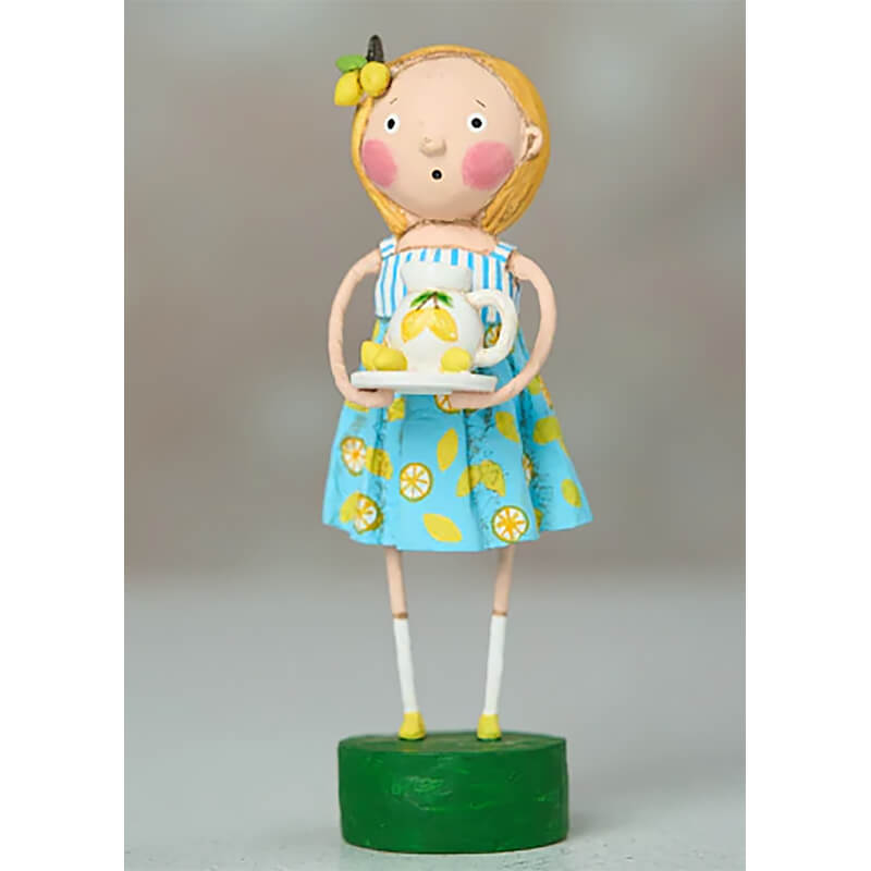 Whimsical folk art doll wearing a blue lemon-print dress and yellow hair bow standing on a green base.