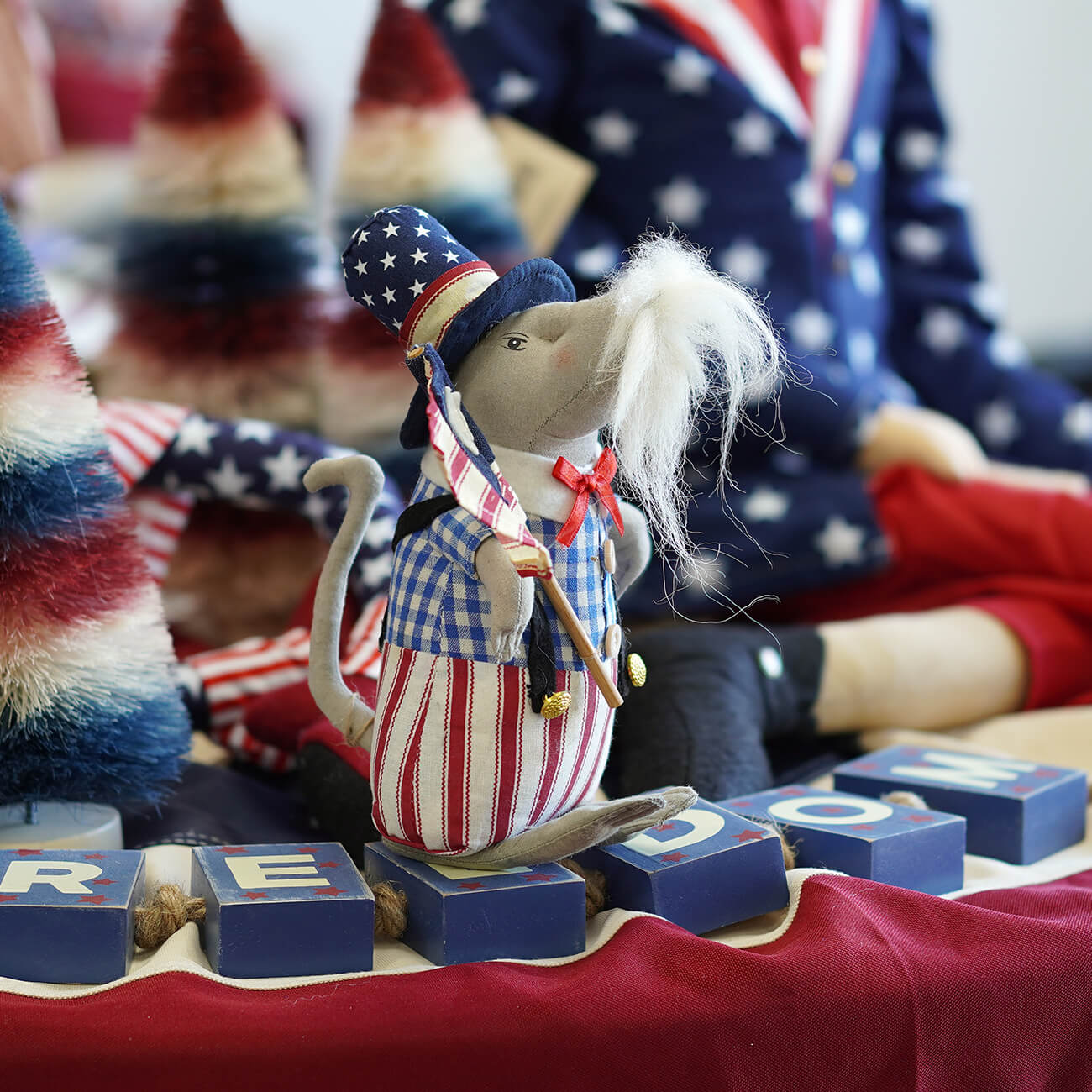 A mouse doll in patriotic outfit with American flag-themed blocks and background