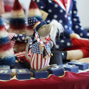 A mouse doll in patriotic outfit with American flag-themed blocks and background