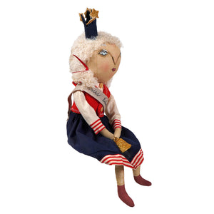 A whimsical little miss liberty doll with curly white yarn hair wearing a navy and red striped dress and gold crown