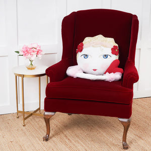 A plush white-faced zombinaland decorative pillow with blonde hair and red flowers on a deep red velvet chair