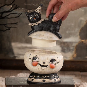 Black cat figurine with white striped party hat on cream moon candle holder in loony jack o lantern decor