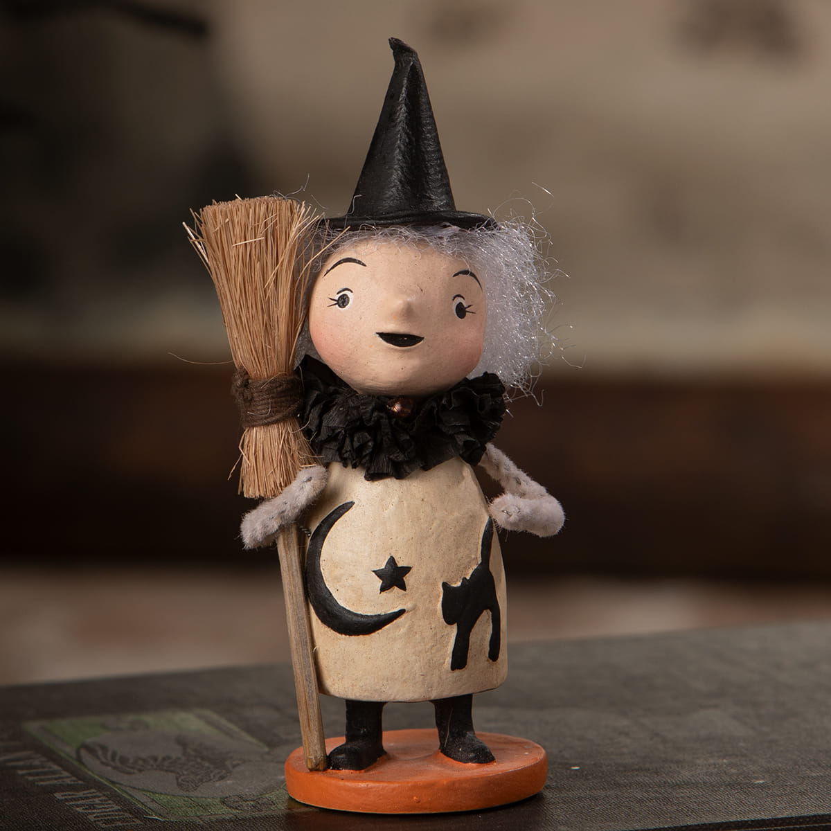 A charming mabel moonspell witch figurine with a black pointed hat white fuzzy hair and cream dress with moon and star design