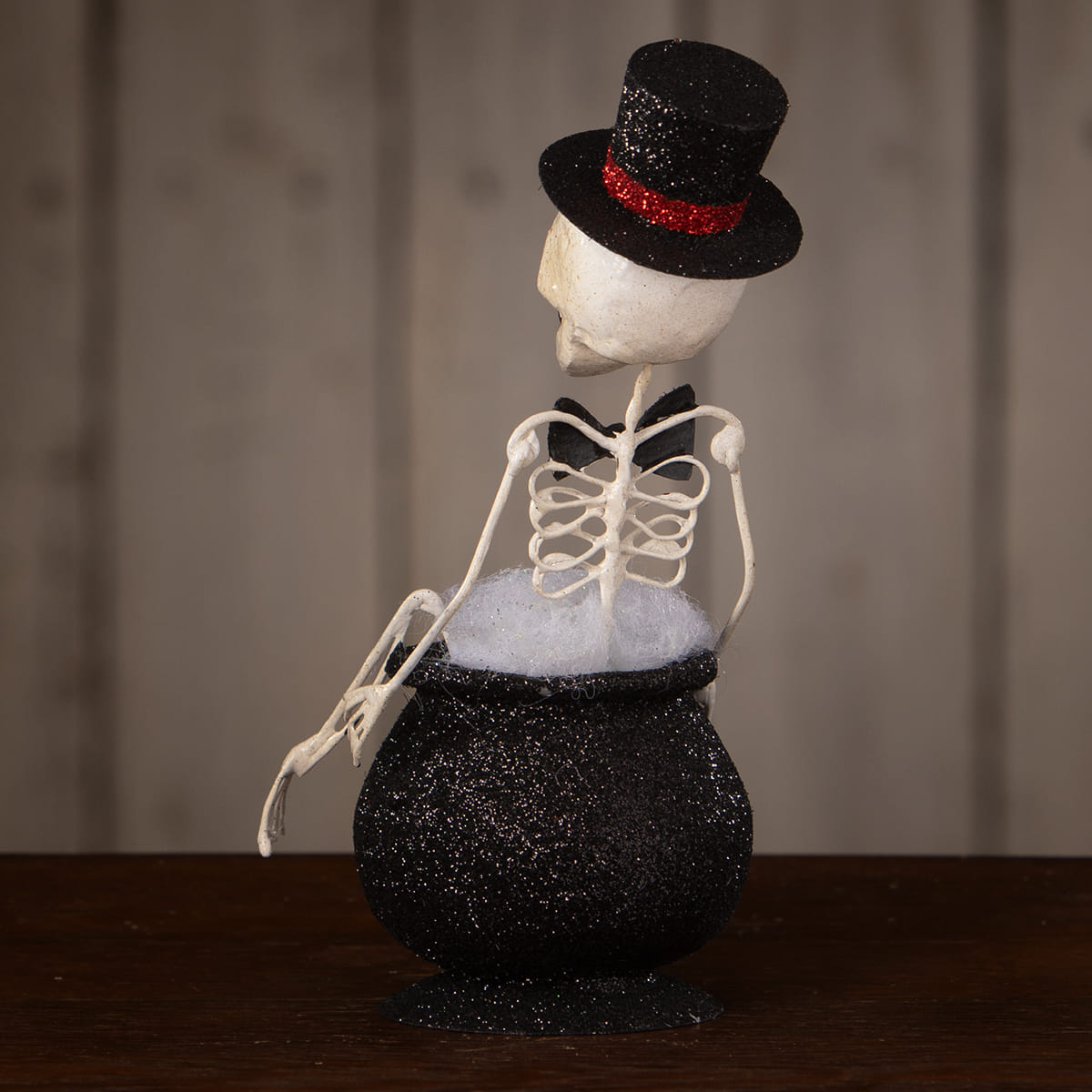 A white skeleton decor figure wearing a black glitter top hat sitting in a black glitter magic cauldron filled with fluff