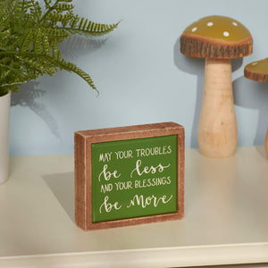A wooden framed sign with green background displaying the text ’May your troubles be less and your blessings be more’