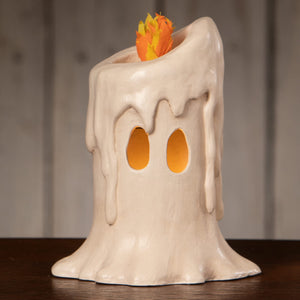 Cream-colored ceramic medium flam’in candle luminary with melting wax drips and glowing orange eye holes
