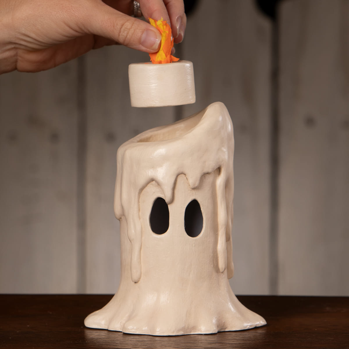 Cream-colored ceramic candle luminary shaped like a melting ghost with black eye holes for spooky decor