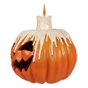 Orange melting midnight glow pumpkin with carved jack o lantern face and white candle dripping wax down sides