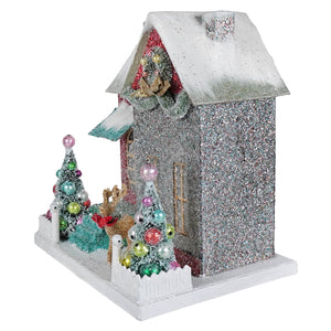 Sparkly silver merry bright glitter cottage with snow-dusted roof, colorful ornament trees, and reindeer figurine nestled nearby