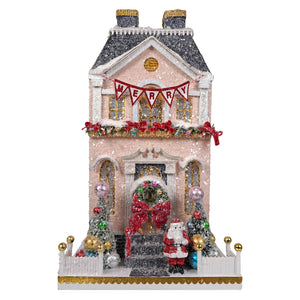 Pink glittered snowy merry manor christmas house ornament with gold roof red merry banner and cody foster santa claus figurine