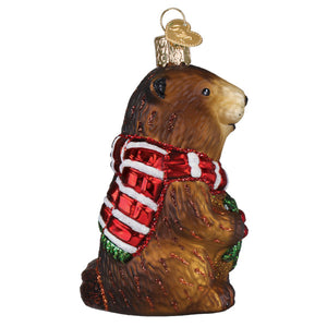 A brown glass christmas ornament featuring a detailed groundhog wearing a red and white striped scarf with glittery accents.
