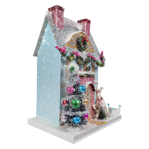 A glittery light blue merry reindeer chateau house ornament with pink chimneys and festive garlands by cody foster