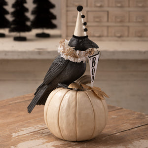 Midnight messenger crow black figurine with white party hat and boo banner on off-white pumpkin for halloween decor