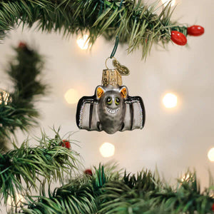 A charming silver glass mini bat ornament with gold tinted ears and eyes hanging on a christmas tree branch