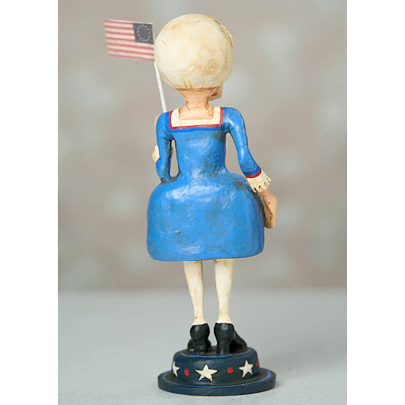 Decorative figurine wearing a blue dress and holding a small American flag.