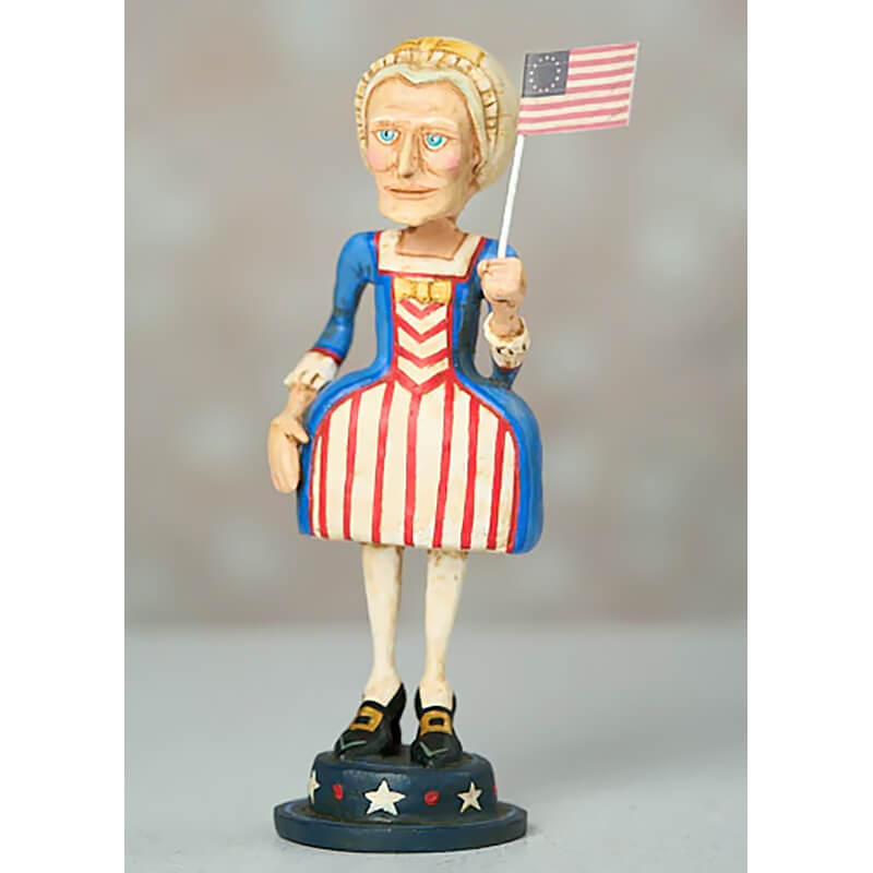 Folk art figurine wearing patriotic American-themed clothing and holding a small American flag.