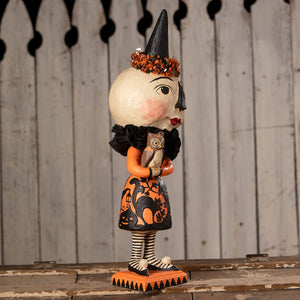 A whimsical miss moon witch figurine with a white head black hat with orange leaves and an orange dress with black cats by bethany lowe halloween