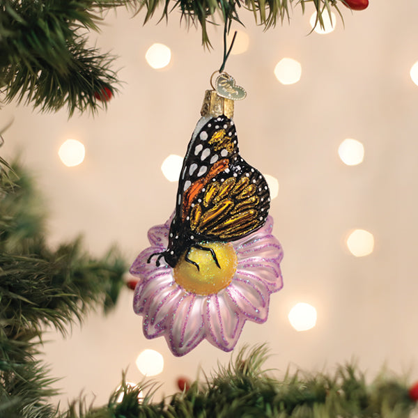 Hand-blown christmas glass ornament of a monarch butterfly with black orange and white wings on a purple flower ornament
