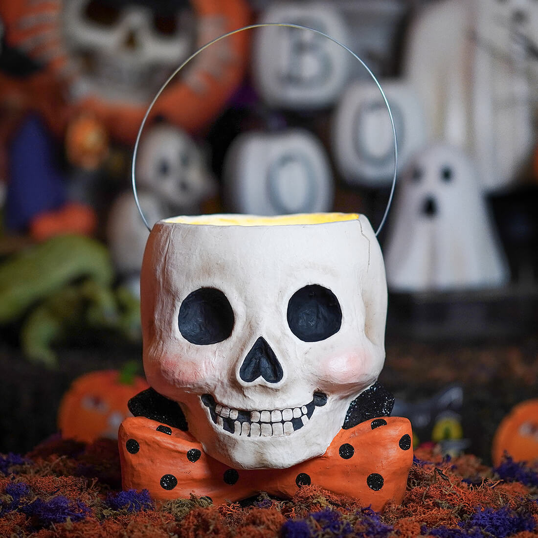A white skull shaped albert skully bucket with black eyes and an orange polka dot bow tie for halloween candy