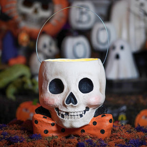 A white skull shaped albert skully bucket with black eyes and an orange polka dot bow tie for halloween candy