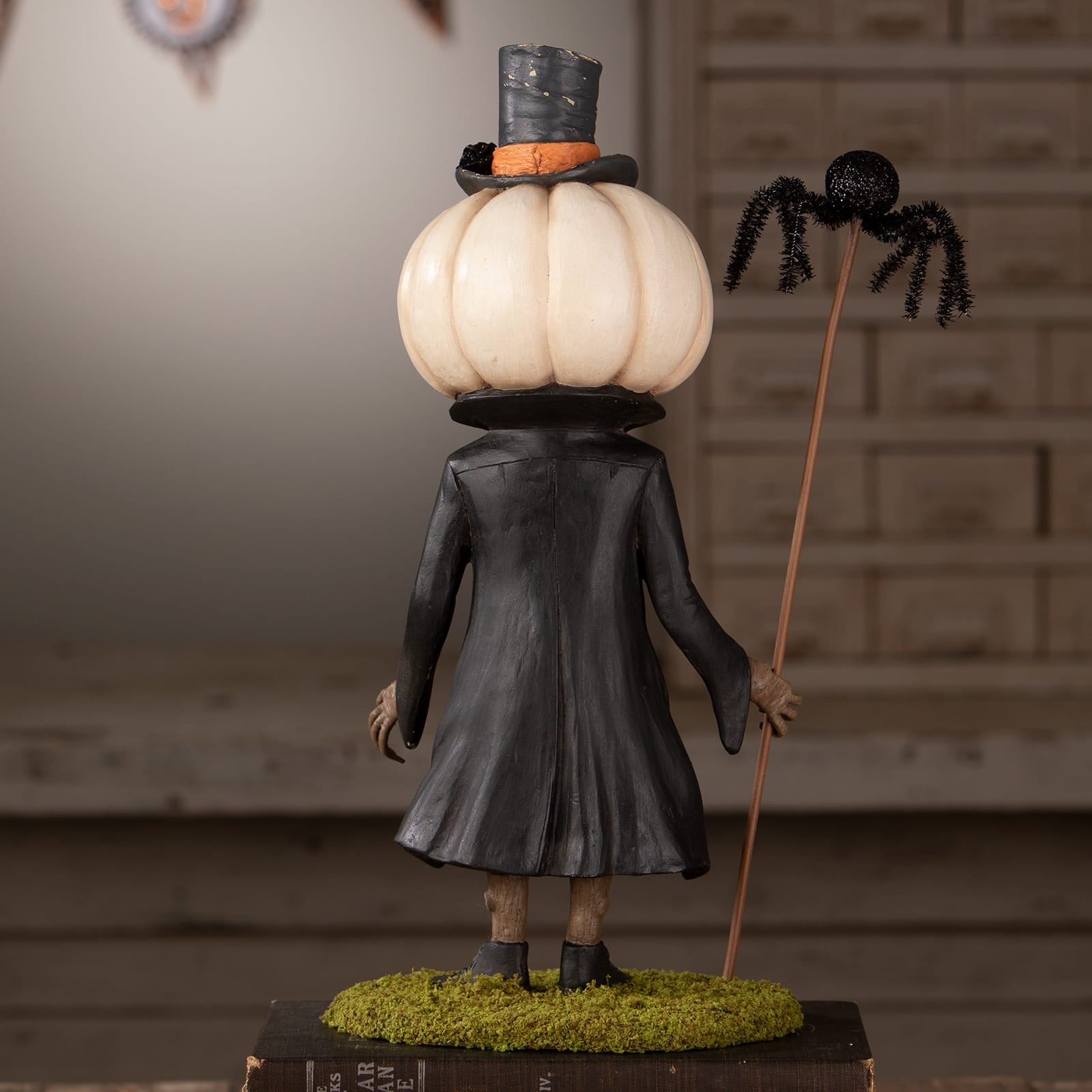 A whimsical halloween figural decor with cream pumpkin head, black top hat, long coat, and spider-topped stick for halloween pumpkins and gourds