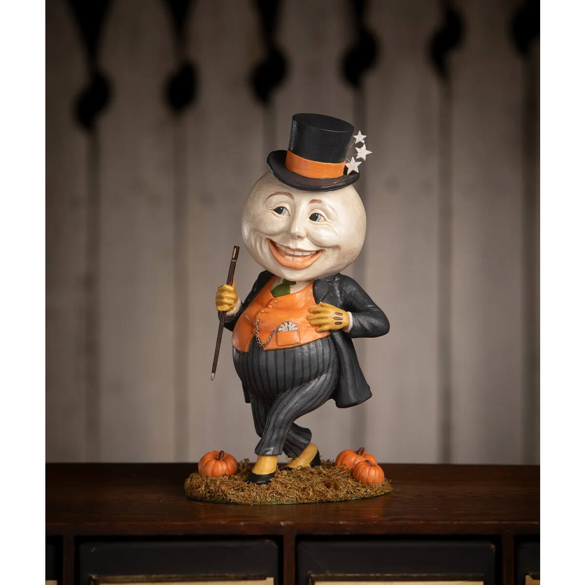 A cheerful harvey moon man pumpkin figure in a black top hat and orange vest standing on hay and pumpkins