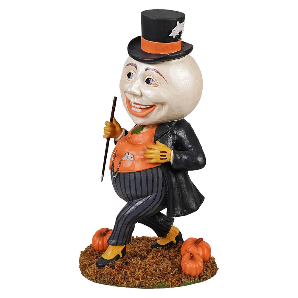 A whimsical harvey moon man figurine with a smiling round head wearing an orange vest and top hat on a pumpkin base