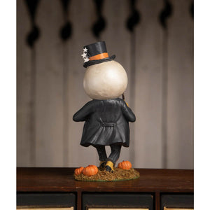 A whimsical harvey moon man pumpkin figure in a black starry top hat and glossy black coat standing on hay with pumpkins