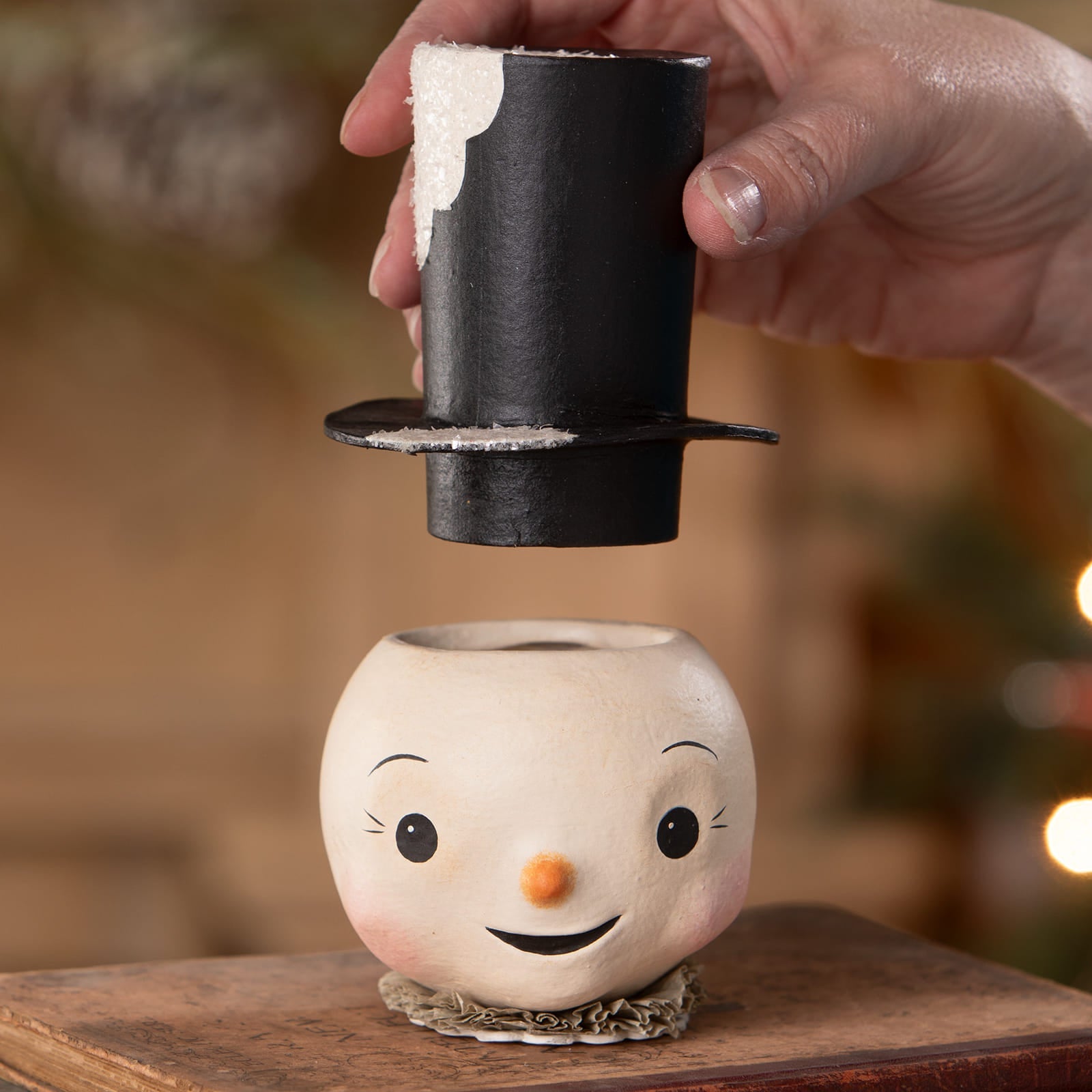 A jolly bobble snowman ceramic planter with a painted face and black top hat being lifted by hand perfect as a christmas snowman container